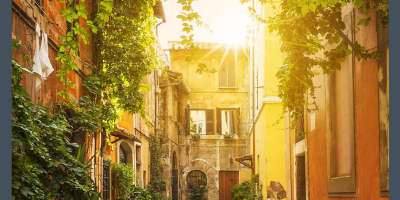 A charming Italian laneway with warm-toned buildings, framed by ivy and with the sun peeking over a three-storey building