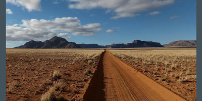 A dirt road cut through desert, leading to a rocky outcrop under a big sky