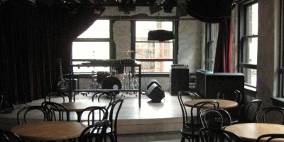 Stage with drum kit, keyboard, gutar and monitors with bistro tables in front